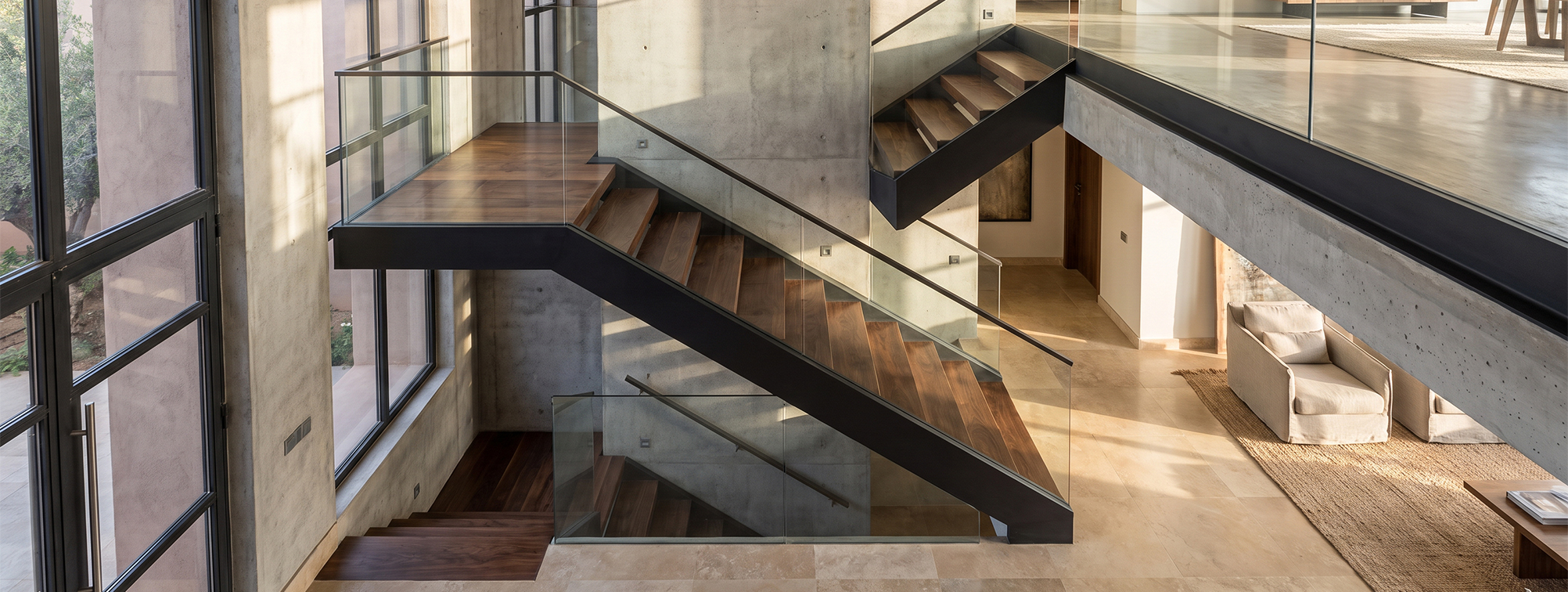 Escalier sur mesure avec structure en acier noir, marches en bois et garde-corps en verre dans un intérieur contemporain