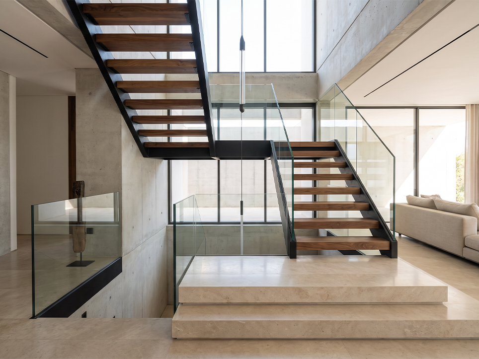 Escalier sur mesure pour villa avec structure en acier noir, marches en bois et garde-corps en verre transparent