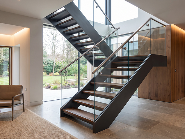 Escalier sur mesure avec structure métallique, marches en bois, garde-corps en verre et main courante en inox poli