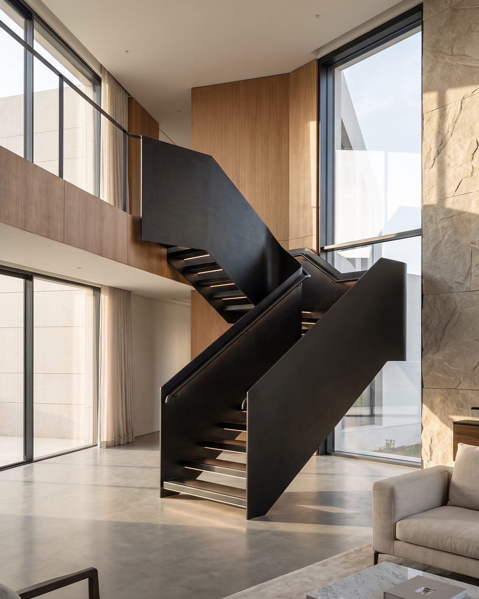 Escalier métallique sur mesure noir à volées tournantes intégré dans une villa contemporaine à double hauteur