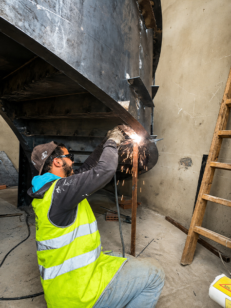 Technicien réalisant une soudure sur la structure métallique courbe d’un escalier sur mesure en chantier